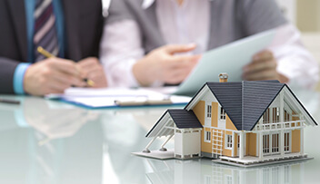 Stock photo - small model of house on table with people reviewing paperwork in the background.