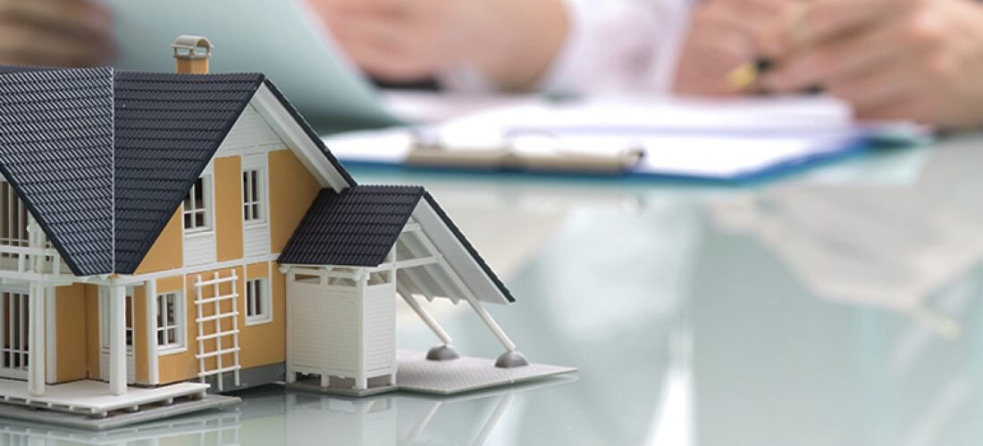 Stock photo - small model of house on table with people reviewing paperwork in the background.