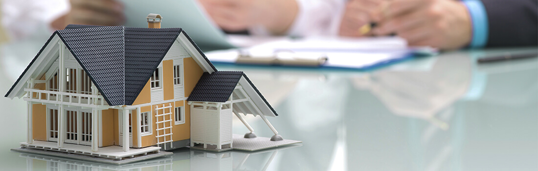 Stock photo - small model of house on table with people reviewing paperwork in the background.